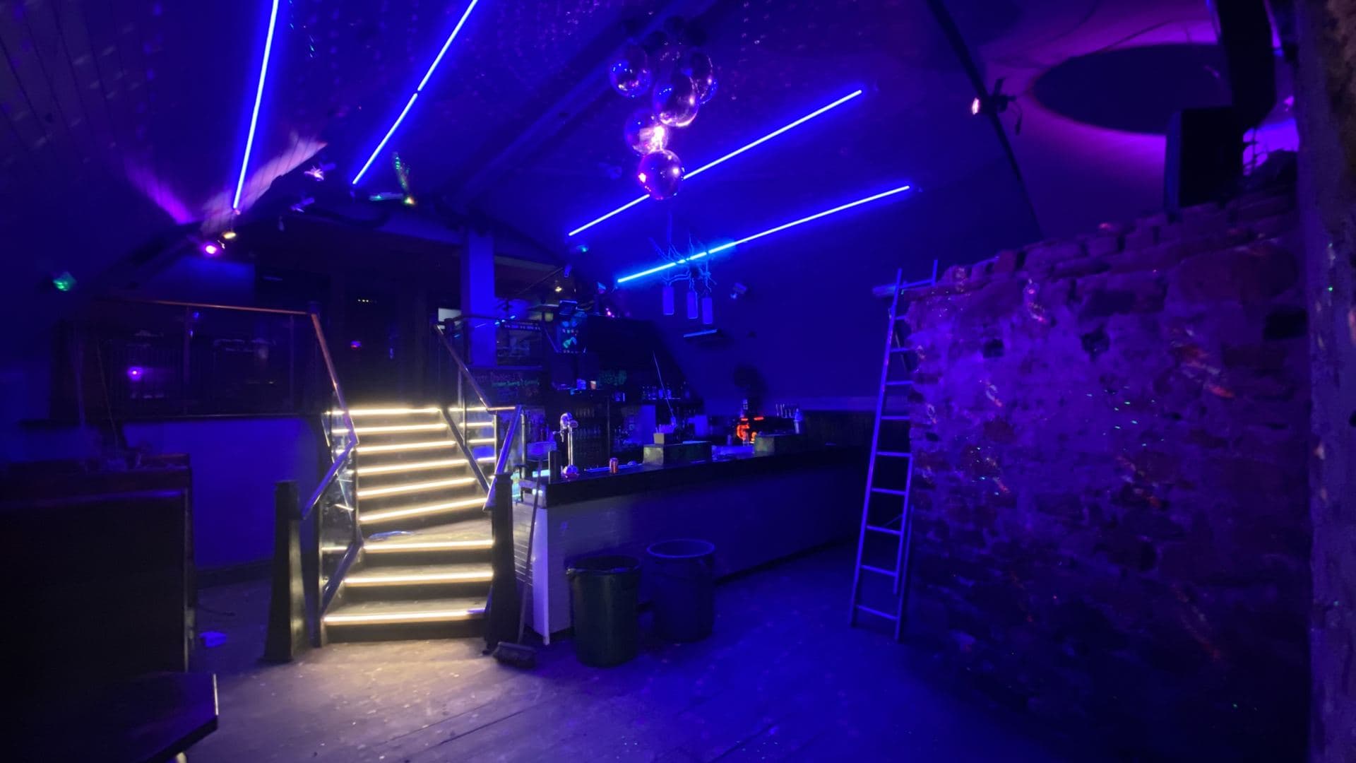 Bar staircase lit with blue neon strip lighting and a mirror ball